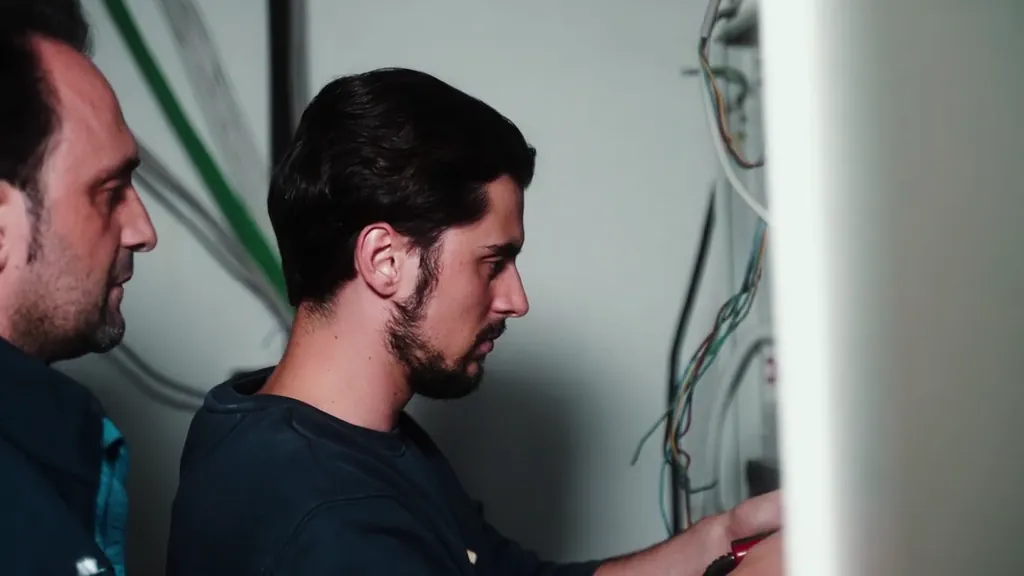 Zwei Mitarbeiter arbeiten an offen liegenden Leitungen in einer Wand