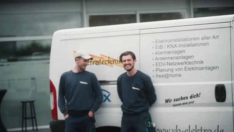 Zwei Mitarbeiter stehen vor dem Firmenwagen, auf dem die Arbeitsgebiete des Betriebs stehen